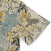 Close-up of a Hawaiian shirt sleeve featuring a floral design with yellow flowers, blue leaves, and subtle black accents on a beige background, emphasizing the shirt&