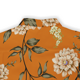 Close-up of a floral shirt with beige flowers and green leaves on an orange background, showcasing detailed petals and stems.