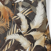 Close-up of a Hawaiian shirt pocket with a jungle-themed design, featuring palm leaves in earthy tones and brown buttons.